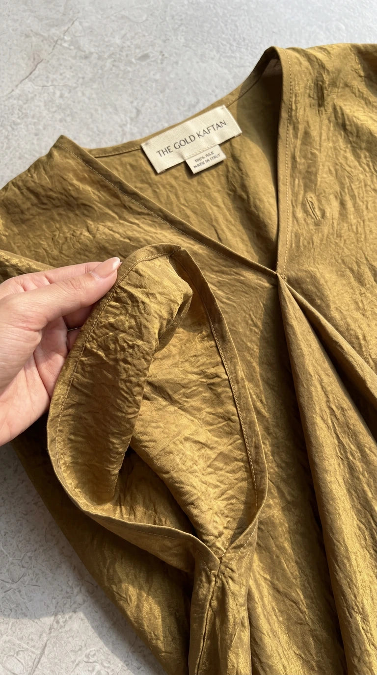 Close-up detail of the textured crinkle fabric and V-neckline of the gold kaftan